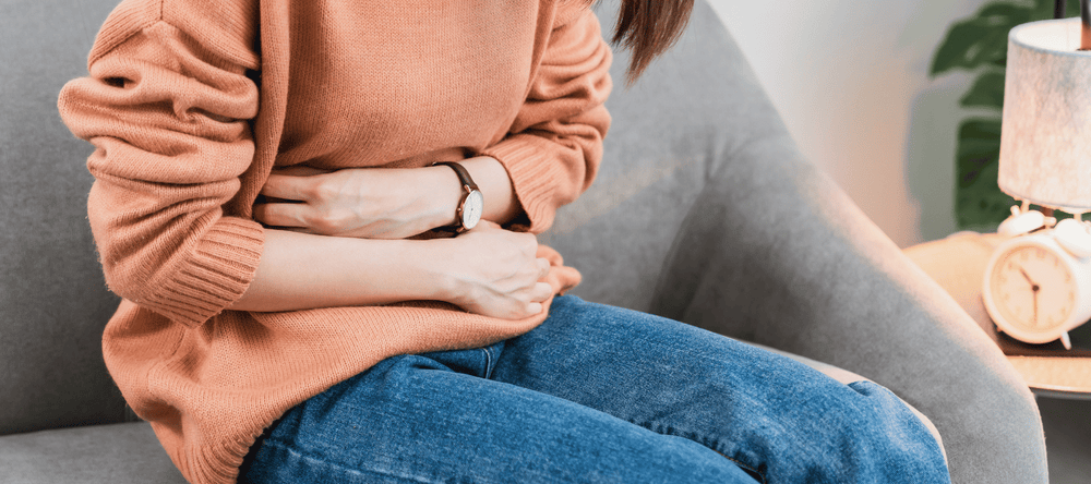 Frau mit Leaky Gut Syndrom die Schmerzen im Bauch hat und sich am Bauch festhält
